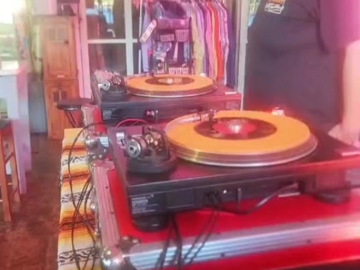 A DJ cutting records on turntables under pink light at Midtown