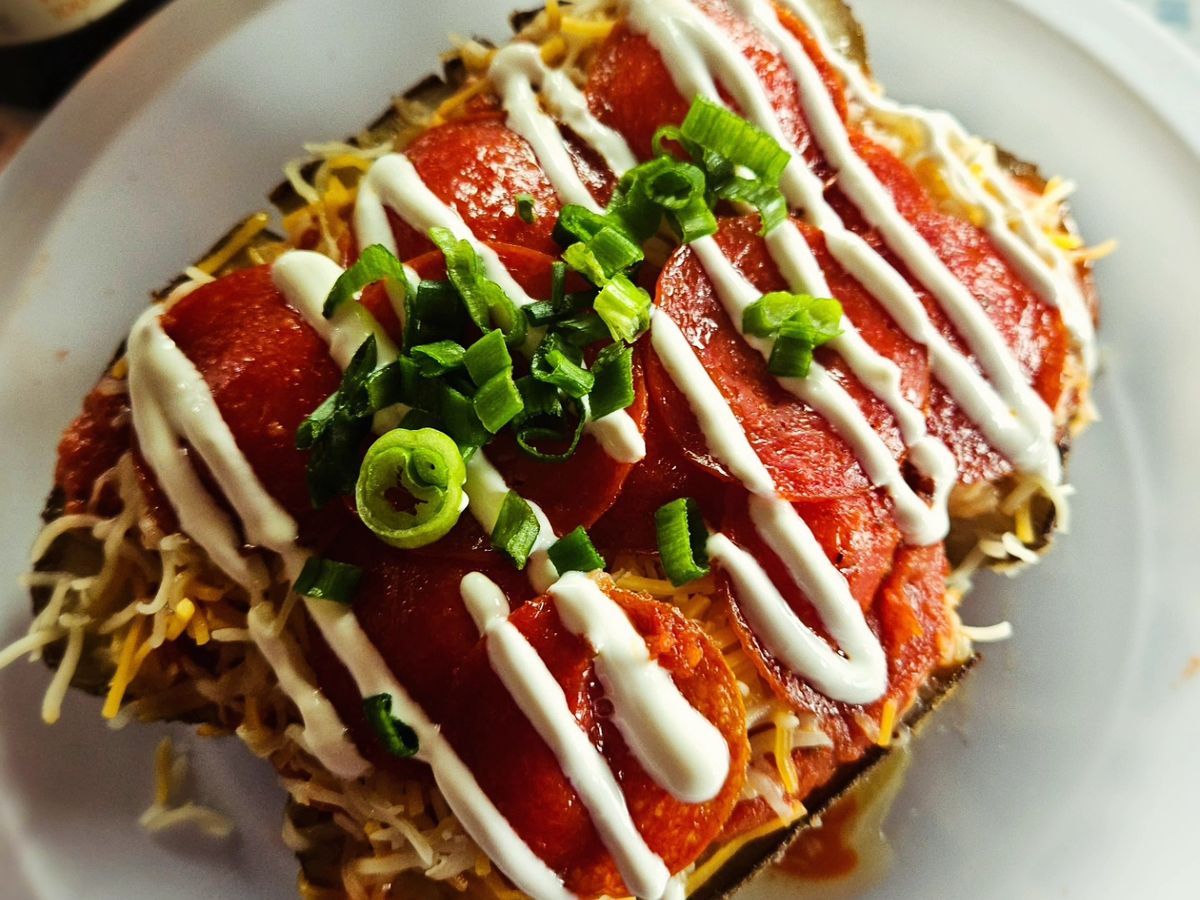 A loaded baked potato topped with chili, cheese, crema and green onions